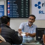 Medewerker van een geldtransferwinkel helpt een klant, met een banner met het Ripple-logo en RLUSD aan de muur