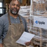 Meubelmaker in een werkplaats staat met een factuur naast verzendklare pallets met de logo's van Ripple en C2FO