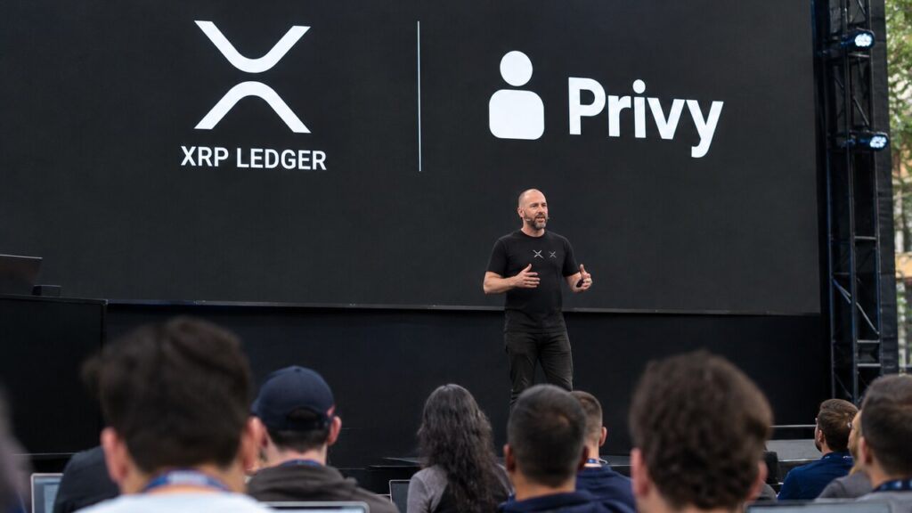 Podium van een ontwikkelaarsconferentie met een groot scherm met de logo's van XRP Ledger en Privy en een spreker voor publiek