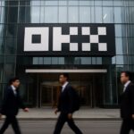 Gevel van een kantoortoren met groot OKX-logo boven de ingang, voetgangers lopen voorbij