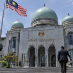 Het Paleis van Justitie in Putrajaya, Maleisië, met een Maleisische vlag en een advocaat met dossiermap op de trappen