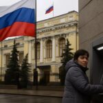 Russische vlag voor het gebouw van de Bank of Russia in Moskou, met op straat een vrouw bij een pinautomaat