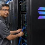 Technicus sluit een kabel aan in een datacenter bij een serverrek met een verlicht Solana-logo