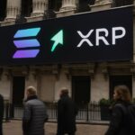 Digitaal scherm op een beursgevel in New York met het Solana-logo groter en groen oplichtend naast het XRP-logo