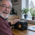 Oudere man met grijze baard zit verrast aan de keukentafel naast een kleine Bitcoin-thuisminer