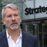 Michael Saylor in donker pak voor de ingang van een gebouw met het Strategy-logo op de gevel