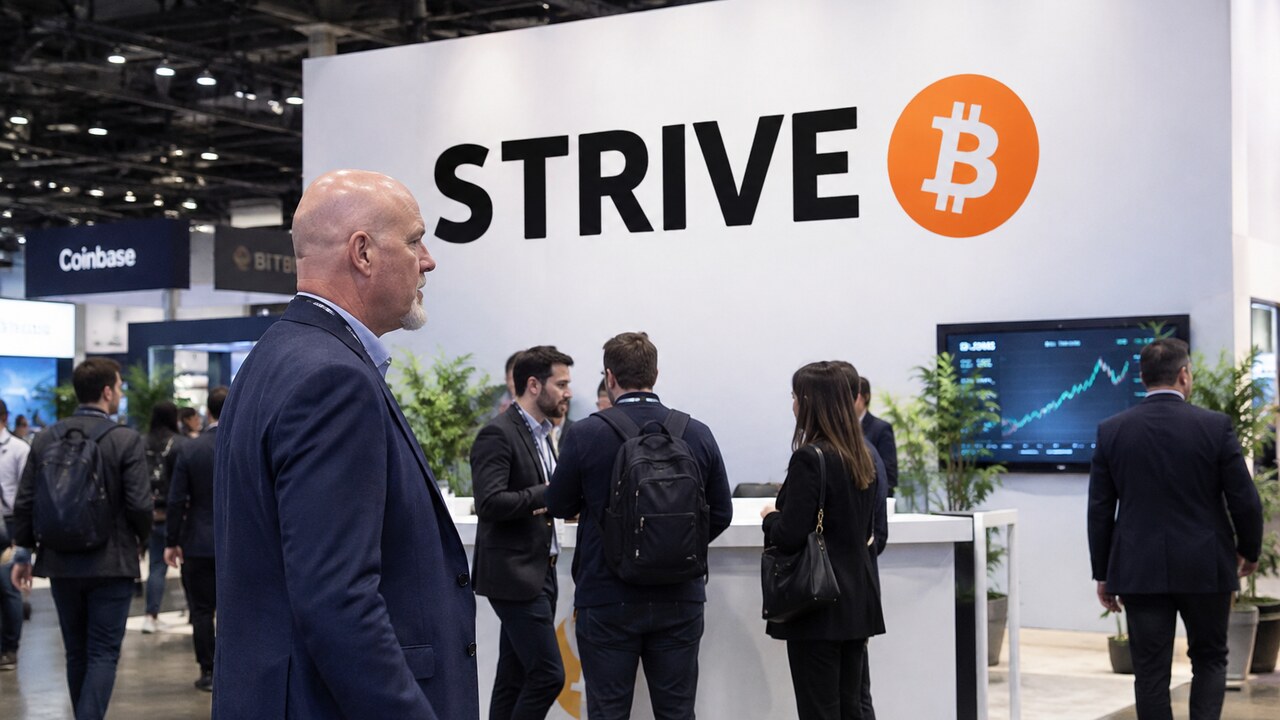 Stand van Strive op een Bitcoin-conferentie met een groot Strive-logo en Bitcoin-symbool, met bezoekers die erlangs lopen