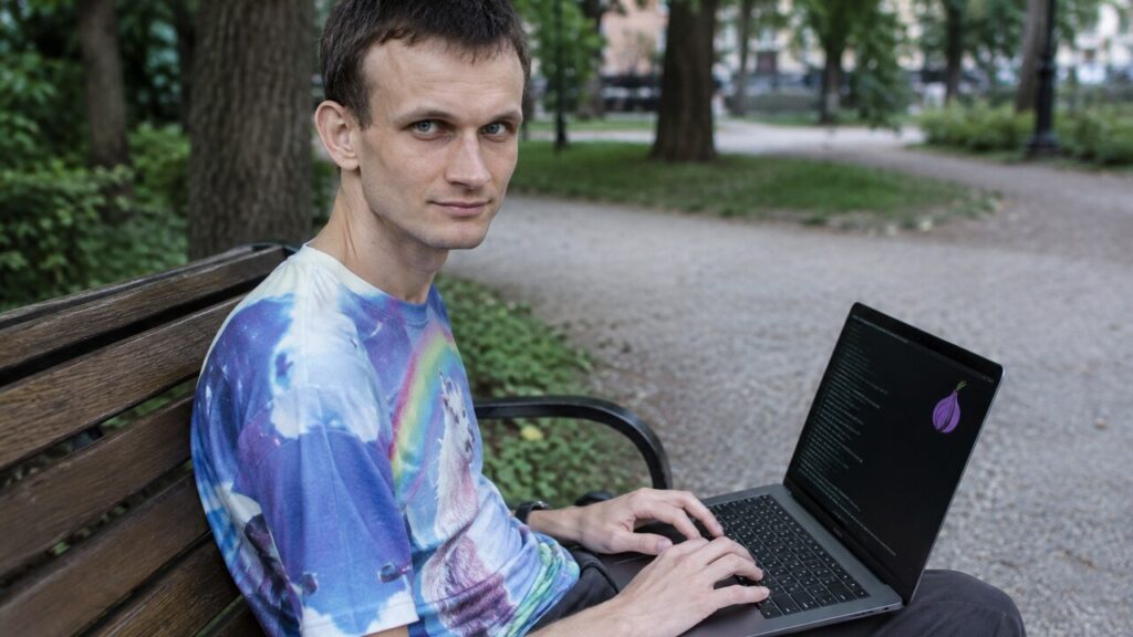 Vitalik Buterin zit op een bankje in een park met een laptop op schoot waarop een terminal met het Tor-logo te zien is