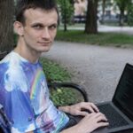 Vitalik Buterin zit op een bankje in een park met een laptop op schoot waarop een terminal met het Tor-logo te zien is