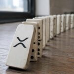 Rij dominostenen op een houten vloer, waarbij de eerste steen met het XRP-logo begint om te vallen