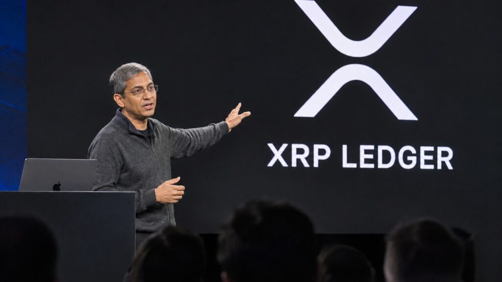 Spreker op een podium van een developerconferentie met het XRP Ledger-logo groot op het scherm achter hem