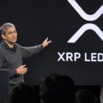 Spreker op een podium van een developerconferentie met het XRP Ledger-logo groot op het scherm achter hem