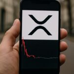 Smartphone in een hand op straat met een handelsapp die het XRP-logo en een tot rust gekomen koersgrafiek na scherpe pieken toont