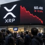 Groot reclamescherm op een druk plein met het XRP-logo en een dalende rode koersgrafiek, met voorbijgangers op de voorgrond