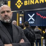 Stand van Binance op een cryptobeurs met een scherm waarop het XRP-logo en een rood dalende koersgrafiek te zien zijn